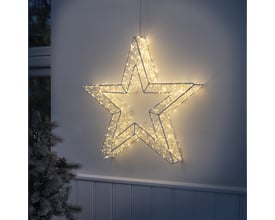 Veli Line metal lys stjerne med 960 varmt hvide LED, monteret på en hvid væg udenfor med en julegren til venstre.
