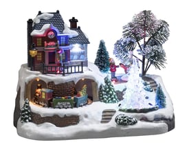 Konstsmide juleby set fra siden, der viser det mekaniske tog, huset, juletræer og snedækket landskab med LED lys.