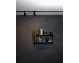 To Astro Ascoli track skinnespots i mat sort aluminium monteret på en sort skinne over en moderne hylde med dekorationer. Spottene giver stemningsfuld belysning.