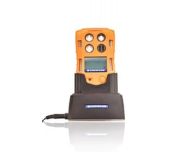 Crowcon T4 gasdetektor i sort bordlader med strømkabel, fotograferet med hvid baggrund og refleksion i overfladen.