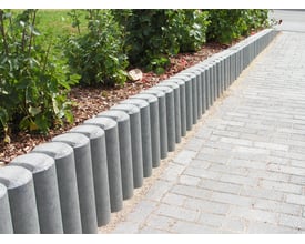 Grå Hanit rund palisade med indhuk, 11 x 80 cm, danner en afgrænsning mellem havebed og flisegang.