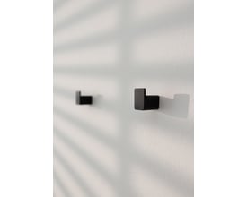 To sorte Metallbude Palo vægknager med en firkantet form, monteret på en hvid væg med skygger fra palmeblade.