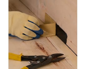 Handskebeklædt hånd anvender NI Metex rottetape til reparation af træværk, med saks i forgrunden.