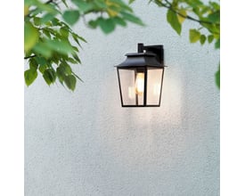 Astro Richmond væglanterne i sort, monteret på en hvid murstensvæg med grønne blade i forgrunden.