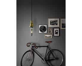 Ledvance 1906 tubular guld LED-pære hængende fra en fatning, med en cykel foran en billedvæg på en grå væg.