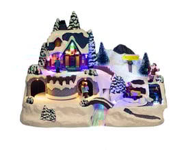 Detaljeret billede af Nordic Winter julebyen "River Town" med sne, lys og figurer af personer og en kane, præsenteret på hvid baggrund.