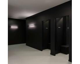 SLV ONE LINEAR 50 WL væglampe monteret på mørk væg i et rum med flere døråbninger og siddepladser.