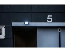 Brennenstuhl 30W LED projektør monteret på en mørk bygningsfacade, lyser op i snevejr ved en port.