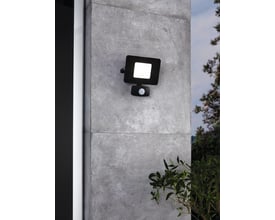 EGLO Faedo 3 udendørs væglampe i sort aluminium med integreret 20W LED og PIR bevægelsessensor, monteret på en grå stenmur med grønne planter i forgrunden.