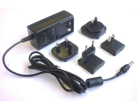 Leica A100 batterioplader til 230V med sort kabel og forskellige internationale stik.