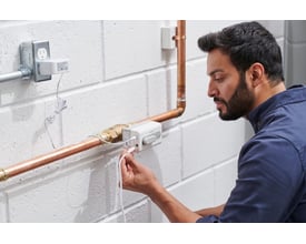 Resideo Braukmann L5 WiFi vandlækagestopventil monteret på kobberrør, mens en mand tilslutter strømkablet.