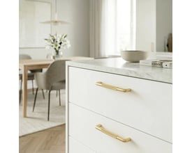 Beslagsboden bøjlegreb i børstet messing, 96 mm, monteret på hvide skuffefronter i et lyst køkken.