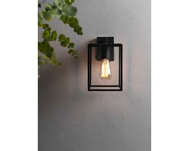 Astro 8048 Box Lantern væglampe i sort sat op på en grå, tekstureret væg med en grøn plante i forgrunden.