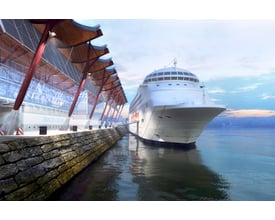 Stor hvid krydstogtskib ved kajen, oplyst af Ansell Lighting Aztec projektør, der belyser havneområdet om aftenen.