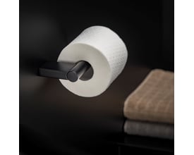 Cosmic toiletpapirholder i sort mat monteret på en væg med et toiletpapirrulle påsat. En håndklæde ses til højre.
