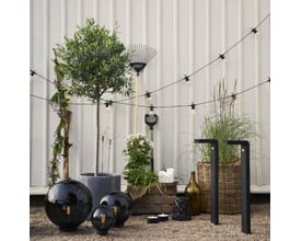 Star Trading Small Circus lyskæde spændt ud over en have med møbler og planter, viser udendørs anvendelse.
