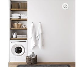 PAX Brisa hvid ventilator monteret højt på væggen over en vaskemaskine og hylder med vasketøj.