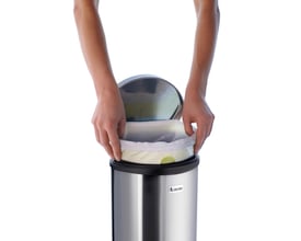 Smedbo outline lite pedalspand i sort belagt rustfrit stål, 6 liters kapacitet, hvor en hånd trækker en plastpose ud.