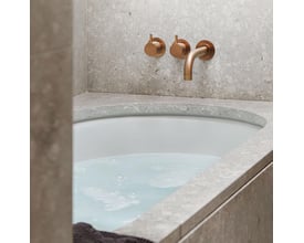 Vola 2-grebsblander med keramiske ventiler i messingfarve monteret over et badekar med vand.