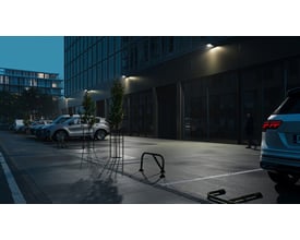 Sort Ansell Lighting WOLF væglampe med skumringsrelæ monteret på bygningsfacade om natten, oplyser en parkeringsplads.