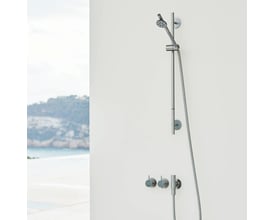 Vola indbygningstermostat med fast afgangsmuffe T60 og håndbruser på en hvid væg, med udsigt til hav og kystlinje i baggrunden.