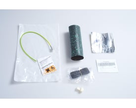 CommScope FOSC-400 kabeltætningssæt til rund port med mørk, cylindrisk varmekrympemuffe, ledning og øvrige dele lagt frem.
