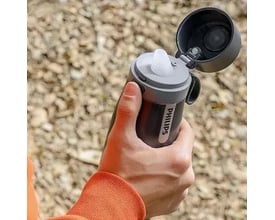 Philips filtreringstermoflaske AWP2771GRR/31 i sort, holdes af en hånd, med drikketud åben, vist udendørs i naturligt lys.