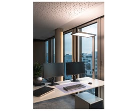 SLV Worklight TL bordlampe i sølv monteret på et skrivebord med to computerskærme. Lampen lyser neutralt hvidt og giver god arbejdsbelysning. Lampen er placeret ved siden af skærmene med udsigt til bygninger gennem vinduet.