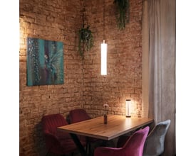 SLV QUIMERA TL bordlampe i mat mørk kobber oplyser et hyggeligt hjørne med røde stole ved et træbord.