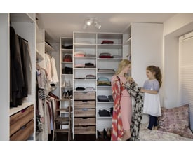 Mor og datter i et walk-in closet, omgivet af tøj og reoler, med fokus på organiseret opbevaring og lys.