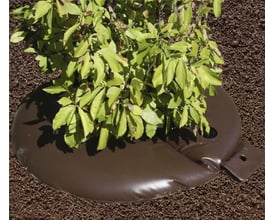 NSH Nordic Byggros vandingspose fyldt med vand omkring en busk, lavet af brunt UV-bestandigt PVC.