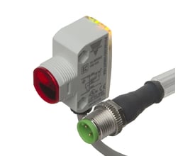 Carlo Gavazzi fotoaftaster PH18CNB20PAT1SA med gråt kvadratisk M18-hoved, rød sensorflade og kabelstik, set skråt.