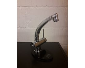Paffoni New Stick DUO krom armatur placeret på en sort bordplade foran en hvid murstensvæg, viser Paffoni logoet.