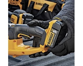 Hænder i arbejdshandsker monterer et DeWalt 18V XR batteri i den gule hækkeklipper.