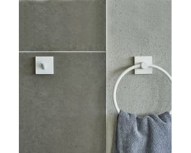 Smedbo House håndklædekrog i mat hvid på en grå betonvæg med en grå frottéhåndklæde hængende på den.