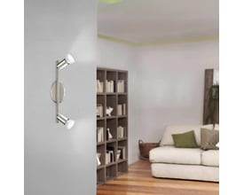 EGLO BUZZ spotlampe i børstet stål med to justerbare lamper, monteret på en grå væg i en stue med en sofa og bogreol.