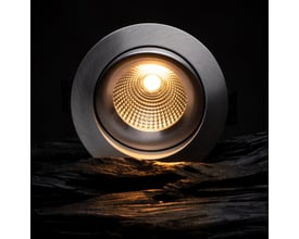 SLC One 360° downlight i aluminium med 8W LED, der lyser varmt hvidt lys op fra en reflekterende inderside på en mørk, træagtig baggrund.