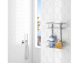 Smedbo Sideline dobbelt brusekurv i poleret krom, monteret på et hvidt sekskantet flisevæg ved siden af et brusehoved og et vindue.