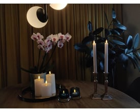 Hyggelig atmosfære med Veli Line 3D T-lys, orkidé og grøn plante i et rum med gyldne gardiner.