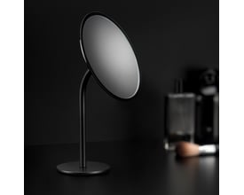 Cosmic fritstående forstørrelsesspejl i sort, Ø20 cm, med elegant fod og baggrund med makeup-tilbehør.