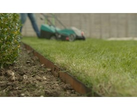 ECCO Products Core Edge kantskinne i corten stål, 1000 mm lang, ses i brug med en plæneklipper bagved på en grøn græsplæne.