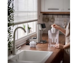 Philips vandautomat ADD5910M/10 med 2,2L kapacitet placeret på køkkenbordet ved vinduet, mens en hånd fylder vand i.