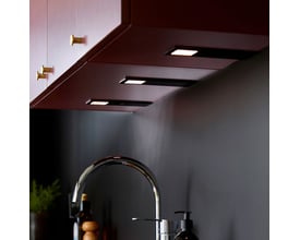 Loevschall Stella spot kit med 3 sorte spots monteret under et mørkerødt overskab over en køkkenvask.