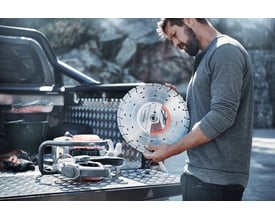 Mand holder Husqvarna diamantklinge Vari-Cut S35 Ø300 mm, klar til brug ved siden af en betonpudser på et lad.