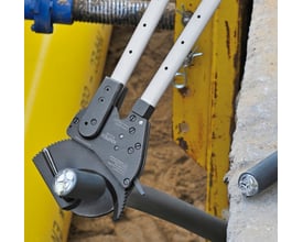 KNIPEX kabelsaks med teleskopskaft klippende i et tykt kabel, med synlige ledninger i det grå kabel.