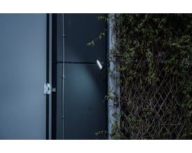 Brennenstuhl LED projektør 100W, der lyser på en mørk facade, fremhæver projektørens kraftige lys og 6500K hvide lysfarve.
