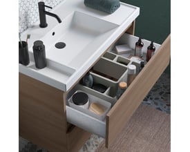 Nærbillede af et åbent Cosmic underskab i valnød, der viser en Teckstone vask med sort armatur og indholdet af to skuffer med opbevaringsbakker.