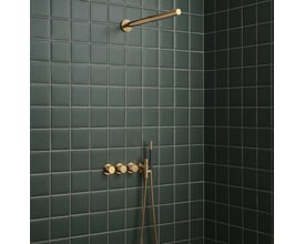 Vola indbygningstermostat med omskifter og håndbruser i guld monteret på mørkegrønne badeværelsesfliser.
