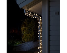 Konstsmide lyskæde med 80 varmhvide LED'er monteret på et tagrende ved en hvid træbeklædt væg om natten.