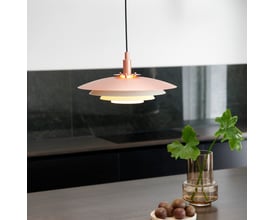 Nordlux Bretagne pendel lampe i kobber med 3 lag skærme, monteret over et mørkt bord med grøn plante og kastanjer.